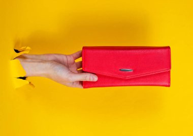 Kırmızı cüzdanı yırtık sarı kağıttan tutan bir kadın. Minimalist yaratıcı moda konsepti
