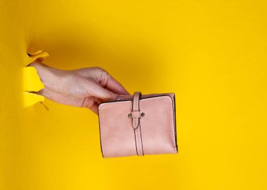 Pembe cüzdanı yırtık sarı kağıtta tutan bir kadın. Minimalist yaratıcı moda konsepti