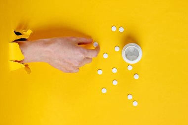 Kadın eli, yırtık sarı kağıdın içinden hap alıyor. Minimalist yaratıcı tıp konsepti