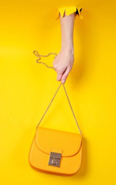 Kadın eli sarı deri çantayı yırtık sarı kağıdın üzerinde tutuyor. Minimalist moda konsepti
