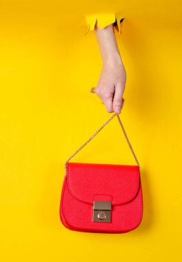 Kadın eli, kırmızı deri çantayı sarı kağıdın üzerinde tutuyor. Minimalist moda konsepti