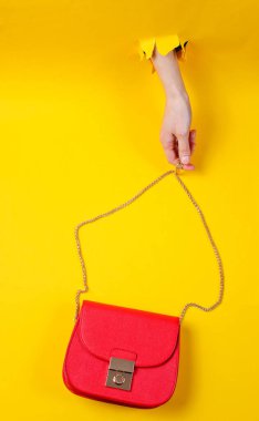 Kadın eli, kırmızı deri çantayı sarı kağıdın üzerinde tutuyor. Minimalist moda konsepti