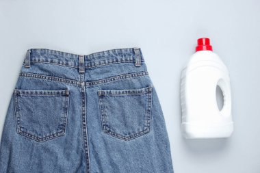 Minimalist çamaşır konsepti. Kot pantolon, gri arka planda bir şişe çamaşır jeli. Üst görünüm