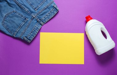 Yıkama konusunda minimalist bir kavram. Fotokopi alanı için kağıt, kot pantolon, mor arka planda bir şişe çamaşır jeli. Üst görünüm