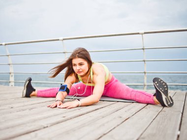 Genç, çekici, formda bir kadın sahilde mindere otururken esneme egzersizleri yapıyor.