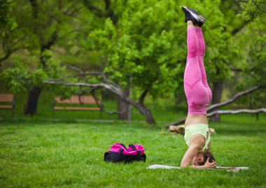 Atletik formda bir kadın, dışarıda parkta kafasının üstünde yoga egzersizleri yapıyor.