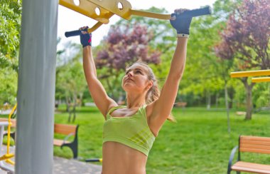 Genç bir kadın kendini parktaki yatay bir çubuğa çekiyor.