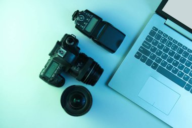 Ekipman profesyonel fotoğrafçısı. Laptop, kamera, lensler ve flaş. Holografik mavi ışık. Üst görünüm