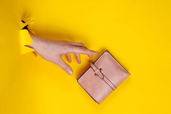 Vrouwelijke Hand Met Roze Portemonnee Door Gescheurd Geel Papier Minimalistisch — Stockfoto