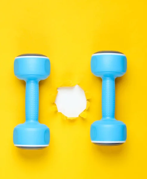 Dumbbells and torn hole in yellow paper. Minimalistic fitness concept. Top view
