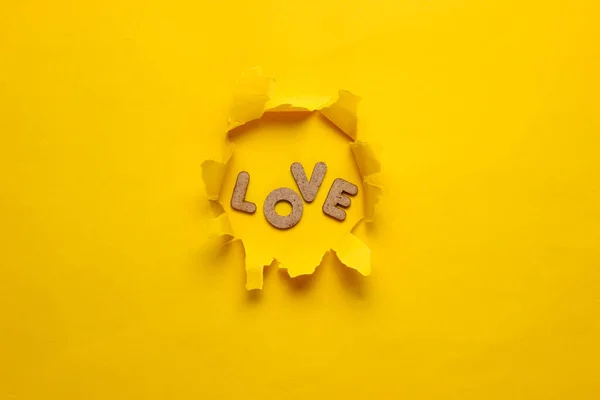 The word love in a torn hole of yellow background. Top view