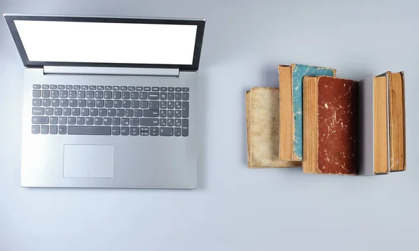 Modern laptop and many old books on a gray background. Old and new sources of information. Top view