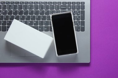 Paketleri açma, tekno blog yazma kavramı. Yeni akıllı telefonlu kutu, mor arka planda dizüstü bilgisayar.