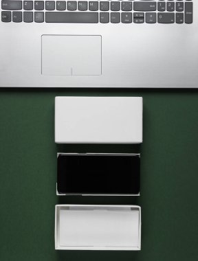 Boksu açma, tekno blog yazma kavramı. Yeni akıllı telefonlu bir kutu, yeşil arka planda dizüstü bilgisayar. Üst görünüm
