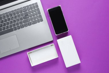 Boksu açma, tekno blog yazma kavramı. Yeni akıllı telefonlu bir kutu, mor arka planda bir laptop. Üst görünüm