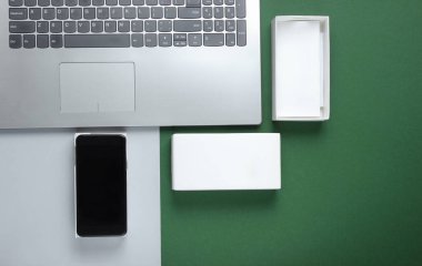 Boksu açma, tekno blog yazma kavramı. Yeni akıllı telefonlu bir kutu, yeşil arka planda dizüstü bilgisayar. Üst görünüm