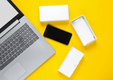 Boksu açma, tekno blog yazma kavramı. Yeni akıllı telefonlu bir kutu, sarı arka planda laptop..