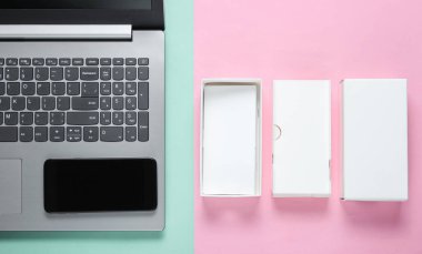 Boksu açma, tekno blog yazma kavramı. Yeni akıllı telefonlu bir kutu, pastel arka planda bir laptop. Üst görünüm