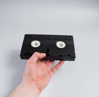 Gri arkaplanda erkek elinde retro video kaseti var.
