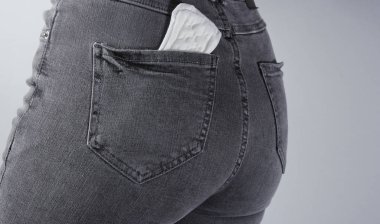 Gri arka plandaki kadın kotunun arka cebinde adet pedi var.