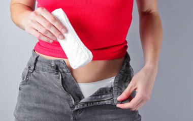 Düğmesiz kotlu bir kadın gri arka planda pedleri tutuyor. Adet günleri konsepti. Kişisel temizlik.