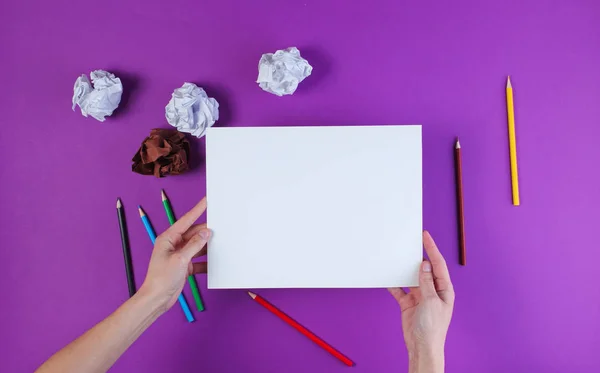 Woman going to draw with colored pencils on a purple background with crumpled paper balls. Top view