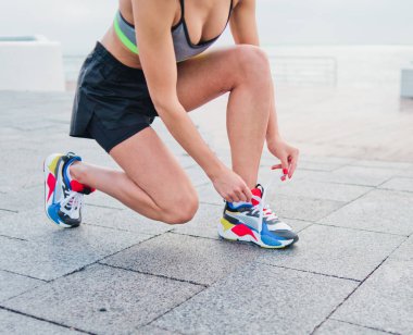 Spor giysili sağlıklı bir kadın beton bir fayansta spor ayakkabı bağcığı bağlıyor ve şehir plajında koşmaya hazırlanıyor.