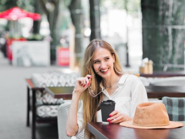 Neşeli, gülümseyen sarışın kadın bir kafede oturur ve kahve içer.