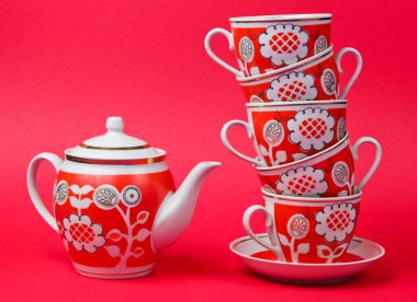 Stack of retro ceramic cups and teapot on red background. Top view