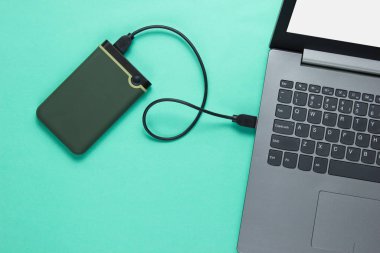 External hard drive connected to laptop on blue background. Top view
