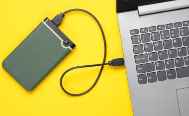 External hard drive connected to laptop on yellow background. Top view