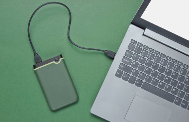 External hard drive connected to laptop on green background. Top view