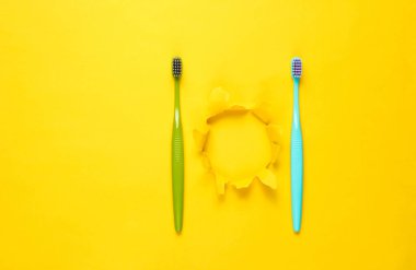 Two New toothbrushes on yellow paper background with torn hole. Minimalism hygiene concept
