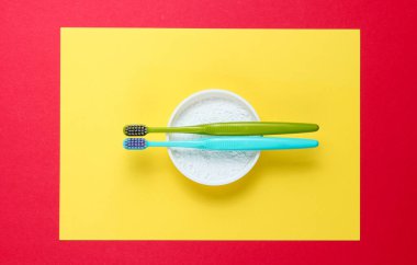 Two toothbrushes, tooth powder on yellow red background. Minimalism oral hygiene concept. Top view