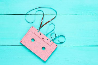 Music lover minimalism concept. Retro style 80s. Pink audio cassette with film on a blue wooden background.