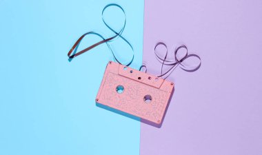Music lover minimalism concept. Retro style 80s. Pink audio cassette with film on pastel paper background. Top view