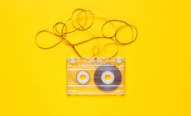 Music lover minimalism concept. Retro style 80s. Audio cassette with film on yellow paper background.