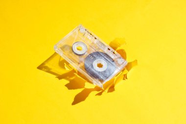 Music lover minimalism concept. Retro style 80s. Audio cassette on yellow paper background with torn hole.
