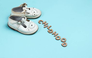 Mavi arka planda çocuk deri sandaletleri ve kelime çocukluğu.