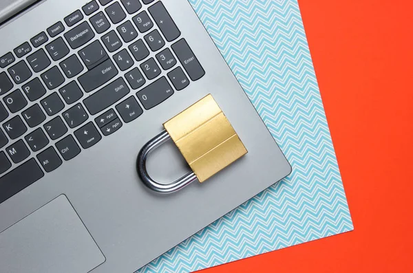 Computer protection concept, internet security. Laptop and lock on orange blue paper background