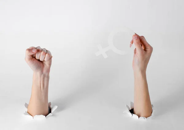 女人的手拿着女权主义的性别符号和拳头穿过白色背景的破洞 创意艺术 — 图库照片