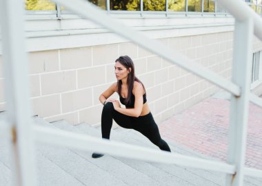 Young fit woman doing stretching legs exercise on stairs outdoors in urban environment