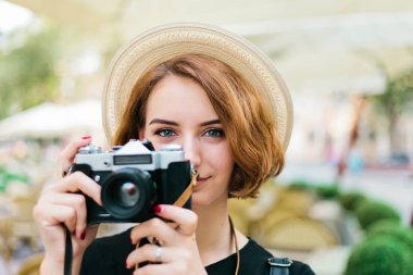 Closeup portrait of a young hipster woman in hat with retro camera outdoors