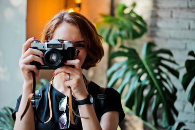 Portrait of a stylish hipster woman with a short haircut with retro camera takes a picture indoors