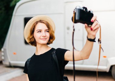 Stylish hipster woman in hat makes selfie portrait using retro camera.