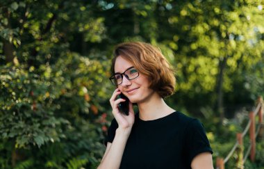 Gözlüklü genç hippi dışarıda telefonla konuşuyor.