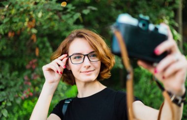Genç ve çekici bir bayan turist, dışarıda retro kamerayla selfie çekiyor.