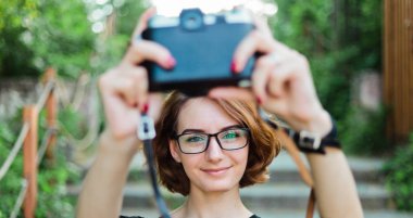 Genç ve çekici bir bayan turist, dışarıda retro kamerayla selfie çekiyor.