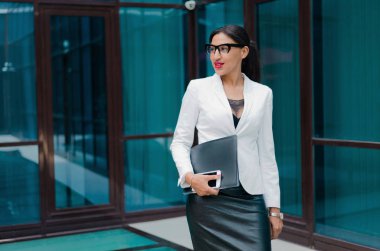 Portrait of a young self-confident afro business woman in a white jacket against the background of a business building outdoors