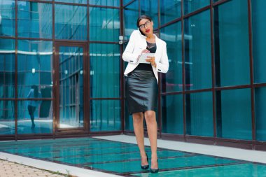 Hepsi çalışıyor. Genç Afro iş kadını telefonda konuşuyor ve iş merkezinin arka planına önemli bilgiler yazıyor.